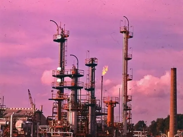 The image shows an oil refinery with lots of pipes and valves, metal poles, metal containers, a...
