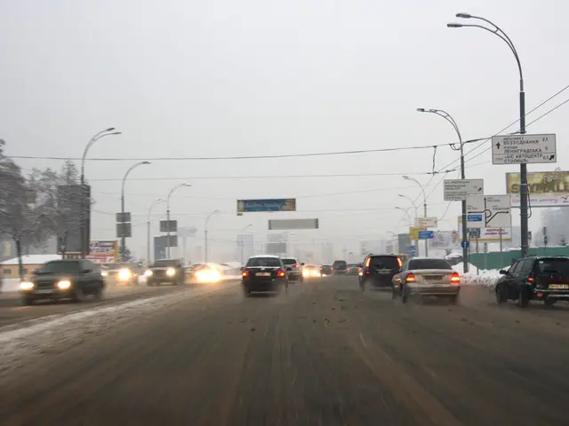 The image shows a city street filled with lots of traffic on a snowy day. We can see vehicles...