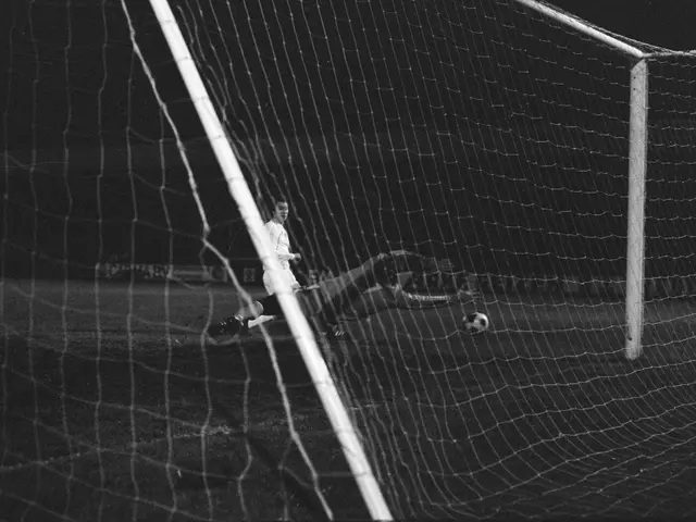 The image shows a black and white photo of a soccer player making a save in front of a goal, with a...