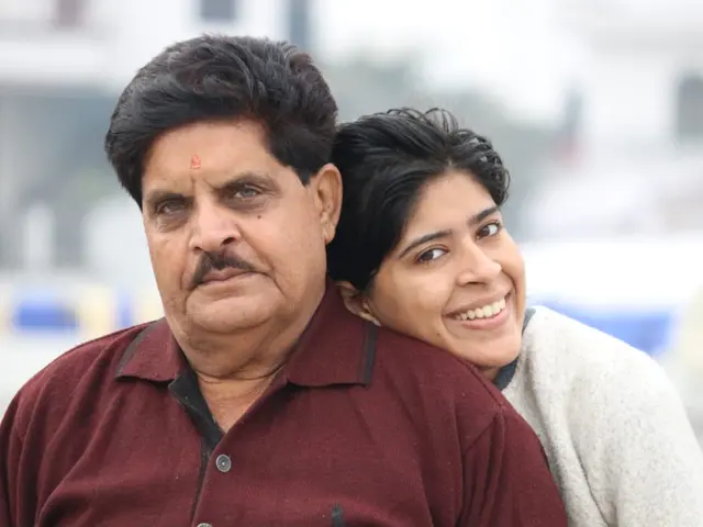 The image shows a man and woman standing next to each other in front of a building, both of them...