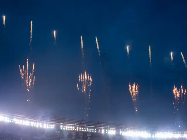 The image shows a football stadium filled with people standing on the ground, illuminated by lights...