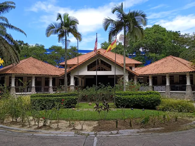 The image shows a large building with a lot of palm trees in front of it, surrounded by flags,...