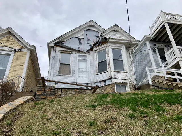 The image shows a house that has been torn down on the side of a hill, surrounded by grass, plants,...