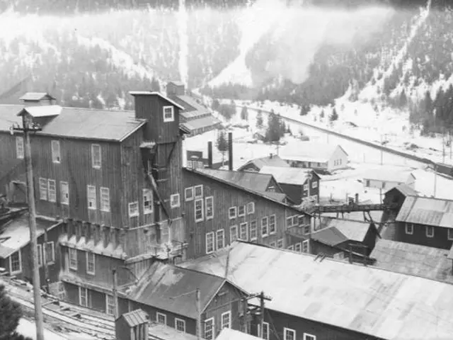 The image shows a black and white photo of a small town in the snow, with a number of buildings,...