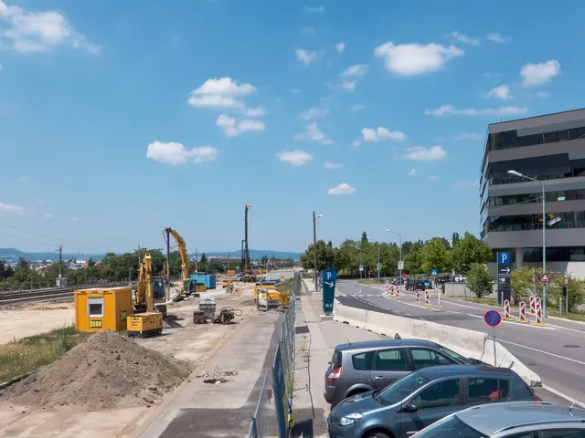 The image shows a construction site with cars parked on the side of the road, surrounded by...