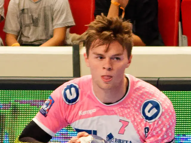 The image shows a man in a pink shirt holding a soccer ball, with another person's hand visible on...