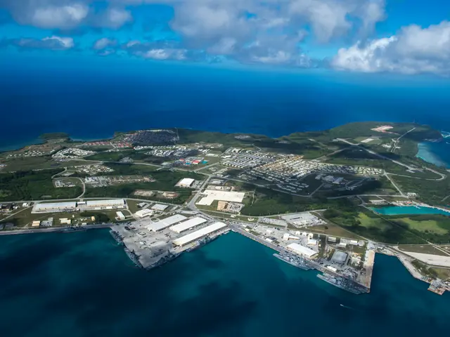 The image shows an aerial view of a small island in the middle of the ocean, with buildings, trees,...