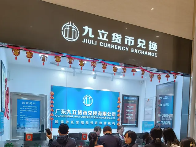 The image shows a group of people standing in front of a counter at the Jiuli Currency Exchange in...