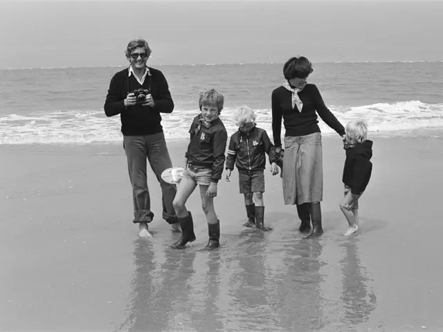 The image shows a black and white photo of a family walking on the beach. The man is holding a...