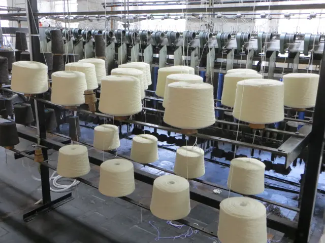 The image shows a factory with a large number of spools of yarn on a spinning machine, surrounded...