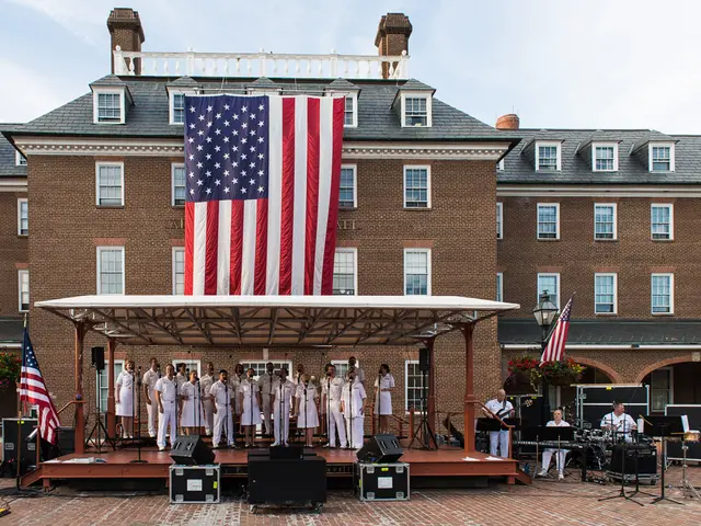 The image shows a group of people standing on top of a stage in front of a building with windows,...