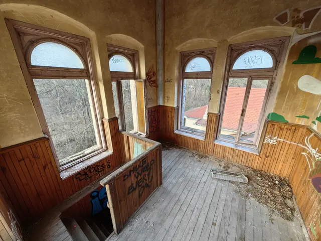 The image shows an abandoned building with graffiti on the walls and windows, a wooden floor, a...