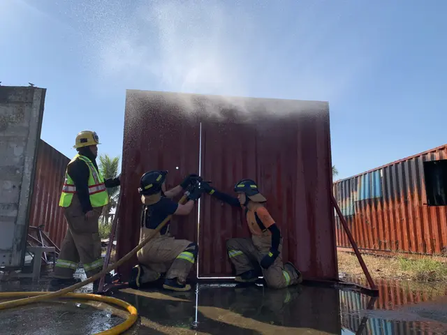 The image shows a group of three firefighters wearing helmets and jackets, one of them holding a...