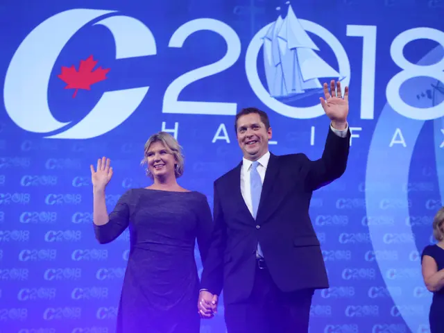The image shows a man and woman standing on a stage in front of a blue screen, both of them...