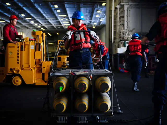 The image shows a group of men in red jackets and blue helmets working on a ship. They are wearing...