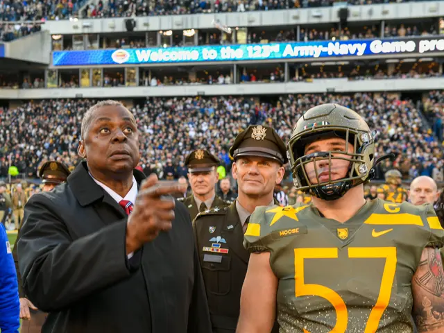 The image shows a man in a suit and tie standing next to a football player wearing a helmet,...