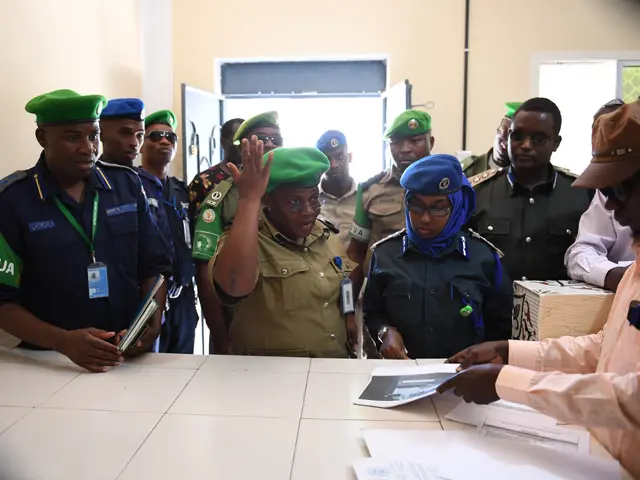 The image shows a group of people standing around a table with papers on it. Some of the people are...