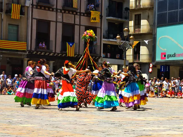 The image shows a group of women in colorful dresses dancing in the street, surrounded by a crowd...