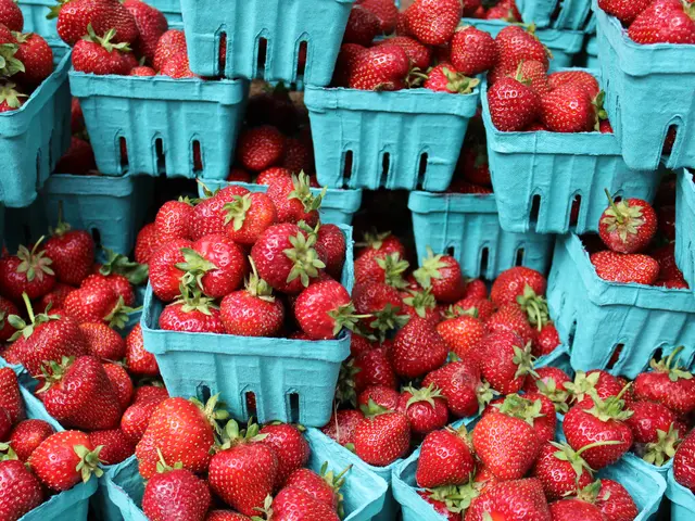 The image shows a farmers market with baskets of ripe, red strawberries stacked on top of each...