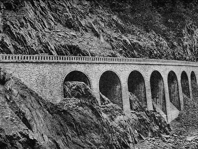 The image shows a black and white photo of a viaduct with arches and pillars, surrounded by rocks...