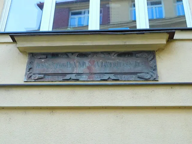 The image shows a building with glass windows and a plaque on the side of it. The plaque reads...