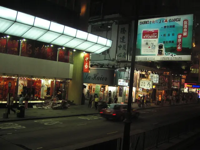 The image shows a bustling city street at night with a car driving down the road, surrounded by...