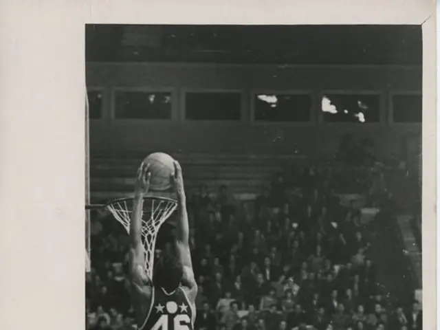 The image shows a black and white photo of a man dunking a basketball in front of a crowd. The man...