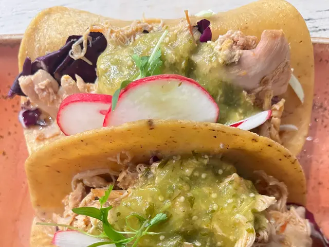 The image shows three tacos on a plate with guacamole and radishes. The tacos are filled with a...