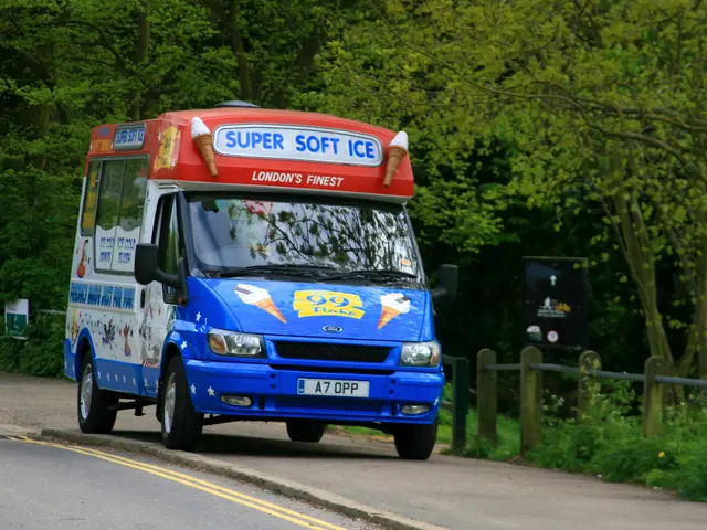 The image shows an ice cream truck driving down a road surrounded by trees, plants, grass, and a...