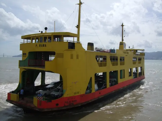 The image shows a large yellow and red ferry boat traveling across a body of water, with a bridge...