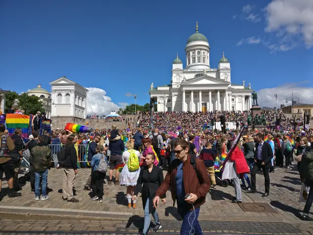 The image shows a large group of people walking down a street in front of a building with windows,...