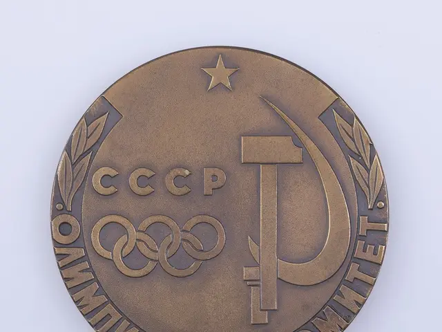 The image shows a bronze medal with the text "Olympic Games" and a hammer and sickle on it, set...