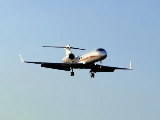 The image shows a private jet flying through a bright blue sky with its landing gear down, gliding...