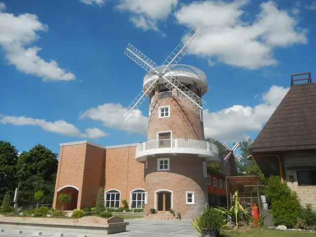 The image shows a windmill in front of a brick building with windows and doors, surrounded by...