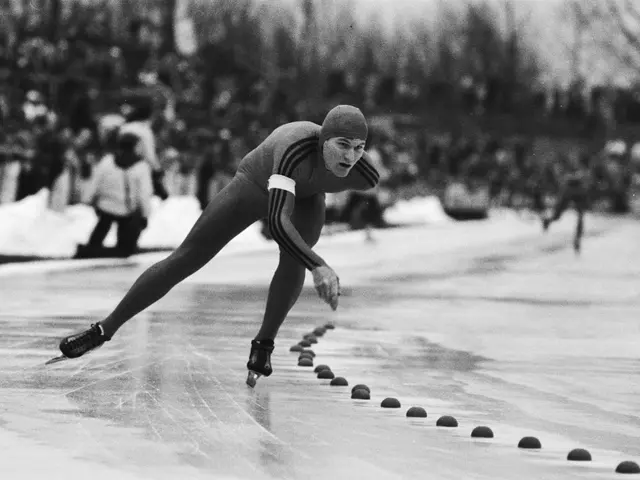 The image shows a black and white photo of a speed skater in action on the ice, wearing a cap and...