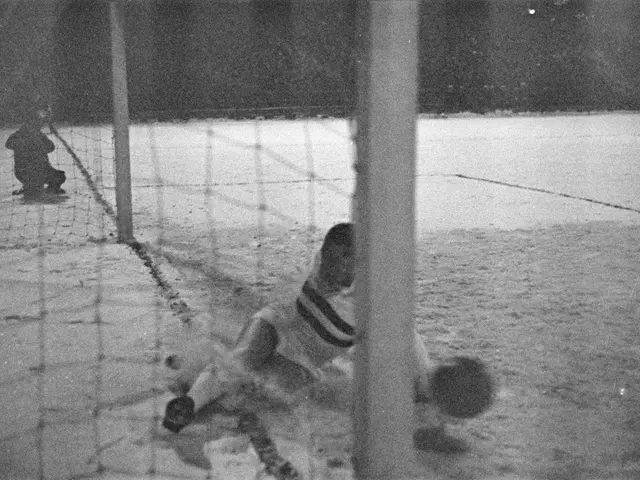 The image shows a black and white photo of two people playing hockey on an ice rink, with a net in...