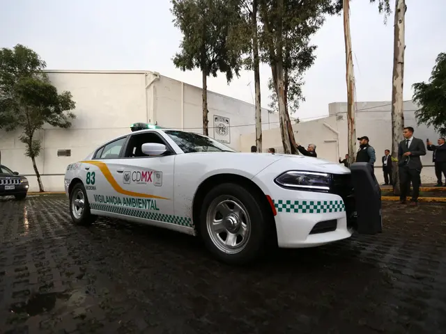The image shows a white police car parked in front of a building, surrounded by a group of people...
