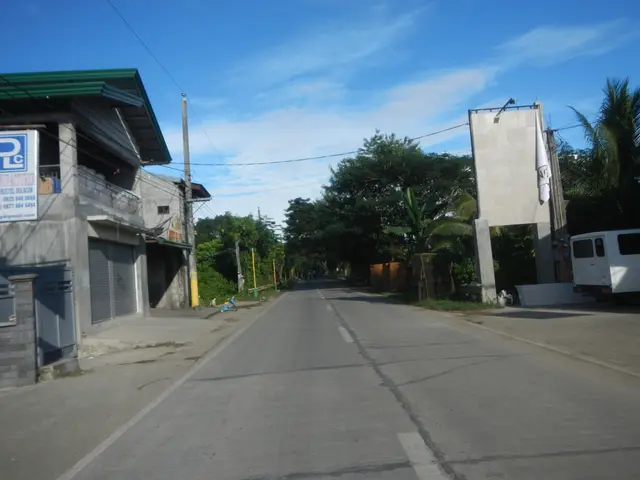 The image shows an empty street with a white van parked on the side of it. On either side of the...