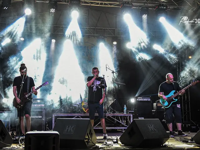 The image shows a group of three men on stage playing guitars and singing into microphones,...