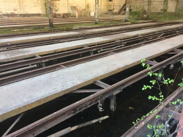 The image shows an old train track in the middle of a city, surrounded by a building with windows,...
