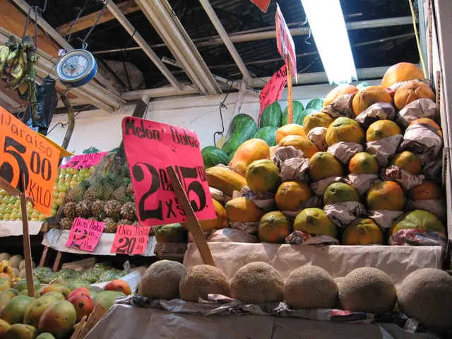 The image shows a market with a variety of fruits on display, including papaya, with price boards...