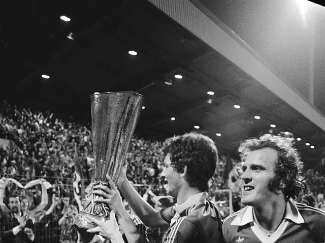 The image shows a group of men holding up a trophy on top of a soccer field, surrounded by a crowd...