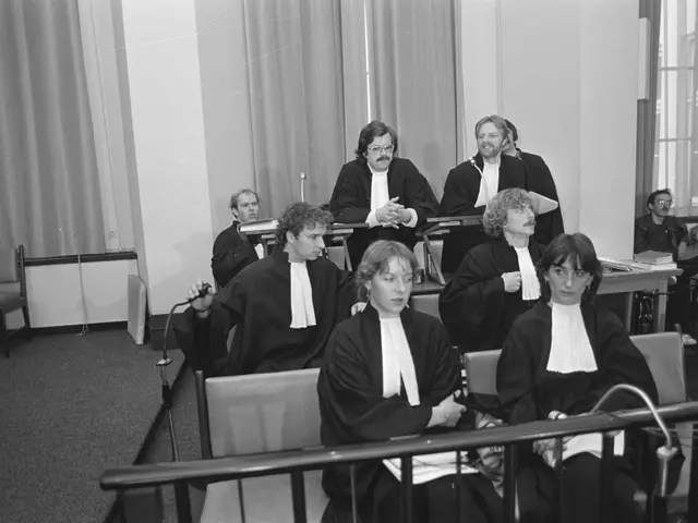 The image shows a group of people sitting in a courtroom, with a railing in the foreground and a...