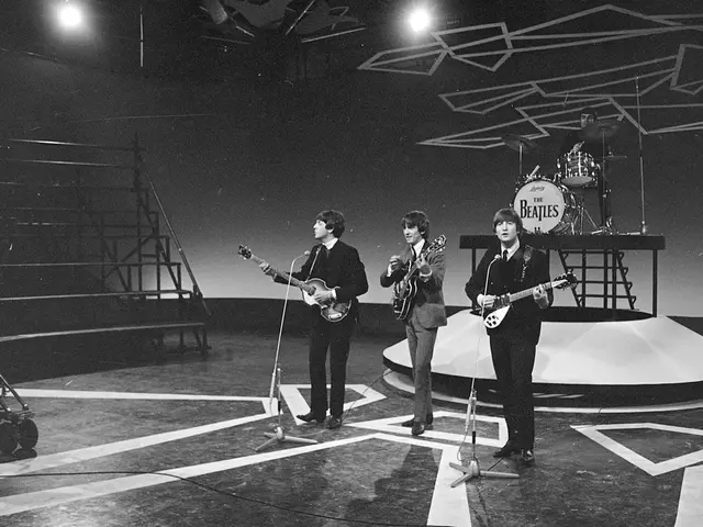 The image shows the Beatles on stage at the Hammersmith Odeon in London, England. The four members...