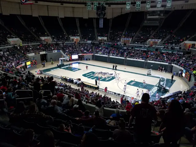 The image shows a large arena filled with lots of people watching a basketball game. There are...