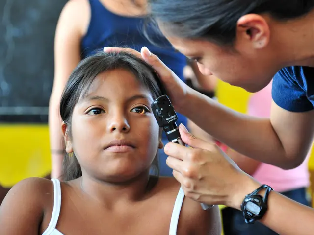 The image shows a young girl getting her ear examined by a doctor wearing a blue t-shirt and a...