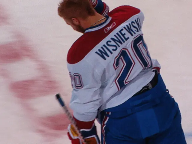 The image shows a hockey player standing on the ice, holding a hockey stick in his hand. He is...