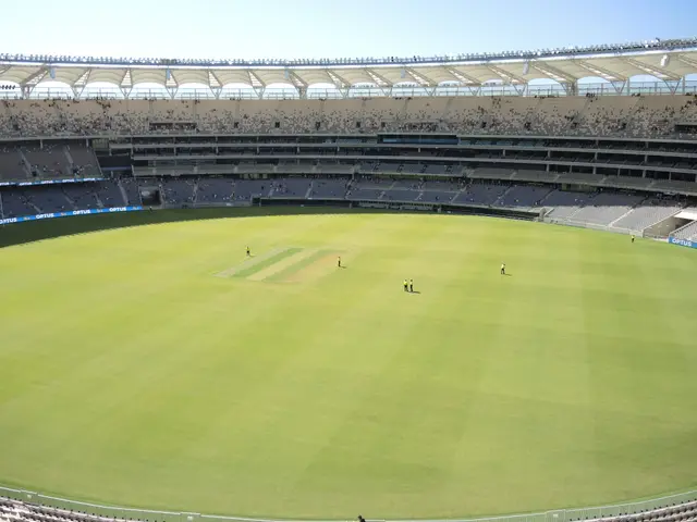 The image shows a large stadium filled with lots of people watching a game of cricket. The ground...