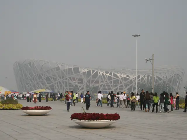 The image shows the Olympic Stadium in Beijing, China. There are many people walking around the...