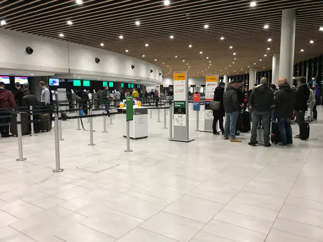The image shows a group of people standing in line at an airport, with some of them holding bags....